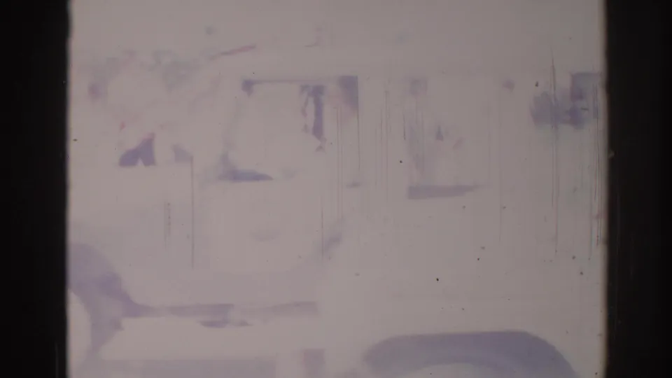 The white truck passes close to camera, with its side and wheel visible through faded 8mm film damage.