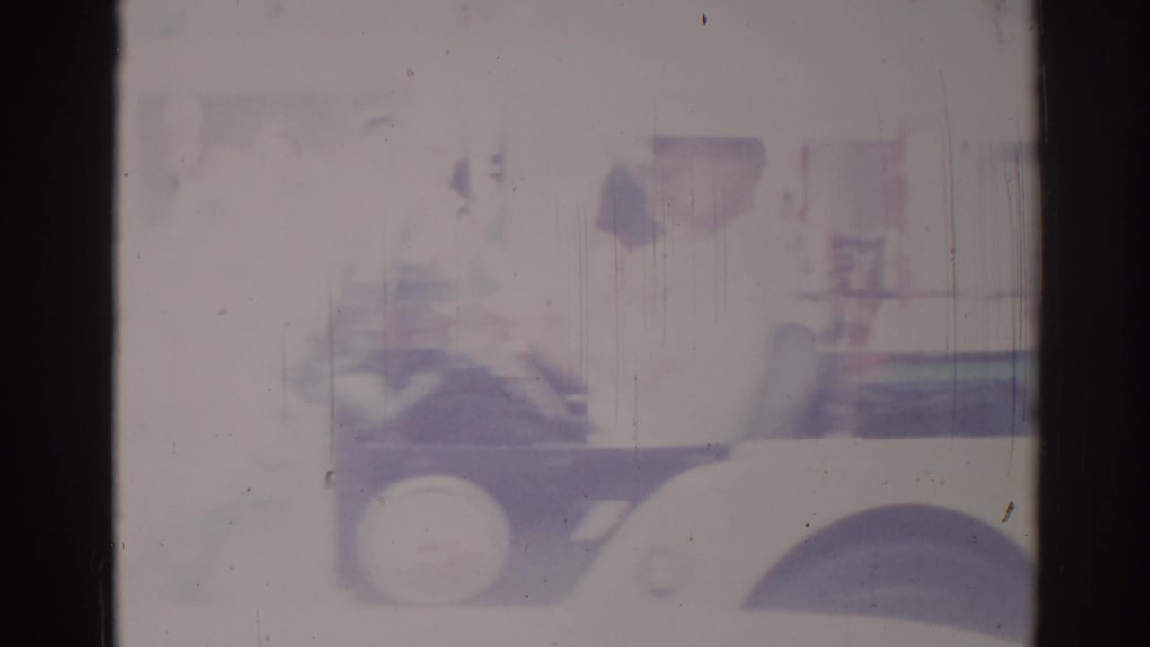 Black truck towing a parade float with a red cow figure, seen through faded 8mm film frames.