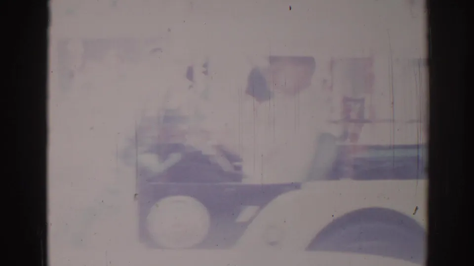 1967 Los Angeles home-movie frame showing a black truck pulling a float with a red cow figure in bright daylight.