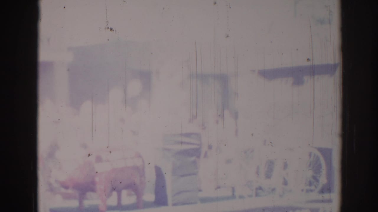 Faded 8mm frame from a Los Angeles parade, showing a red cow figure on a float near a dark truck.