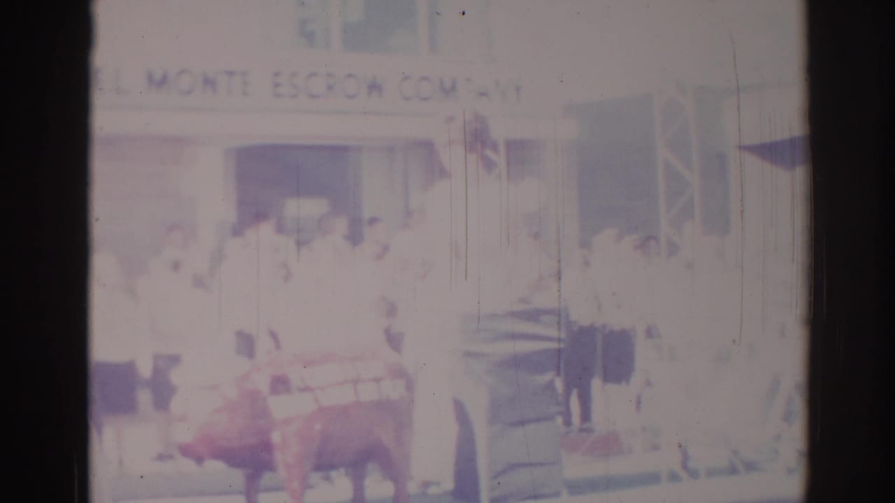 1967 Los Angeles street-parade frame with spectators, Monte Escrow Company signage, and the red cow float at the lower edge.
