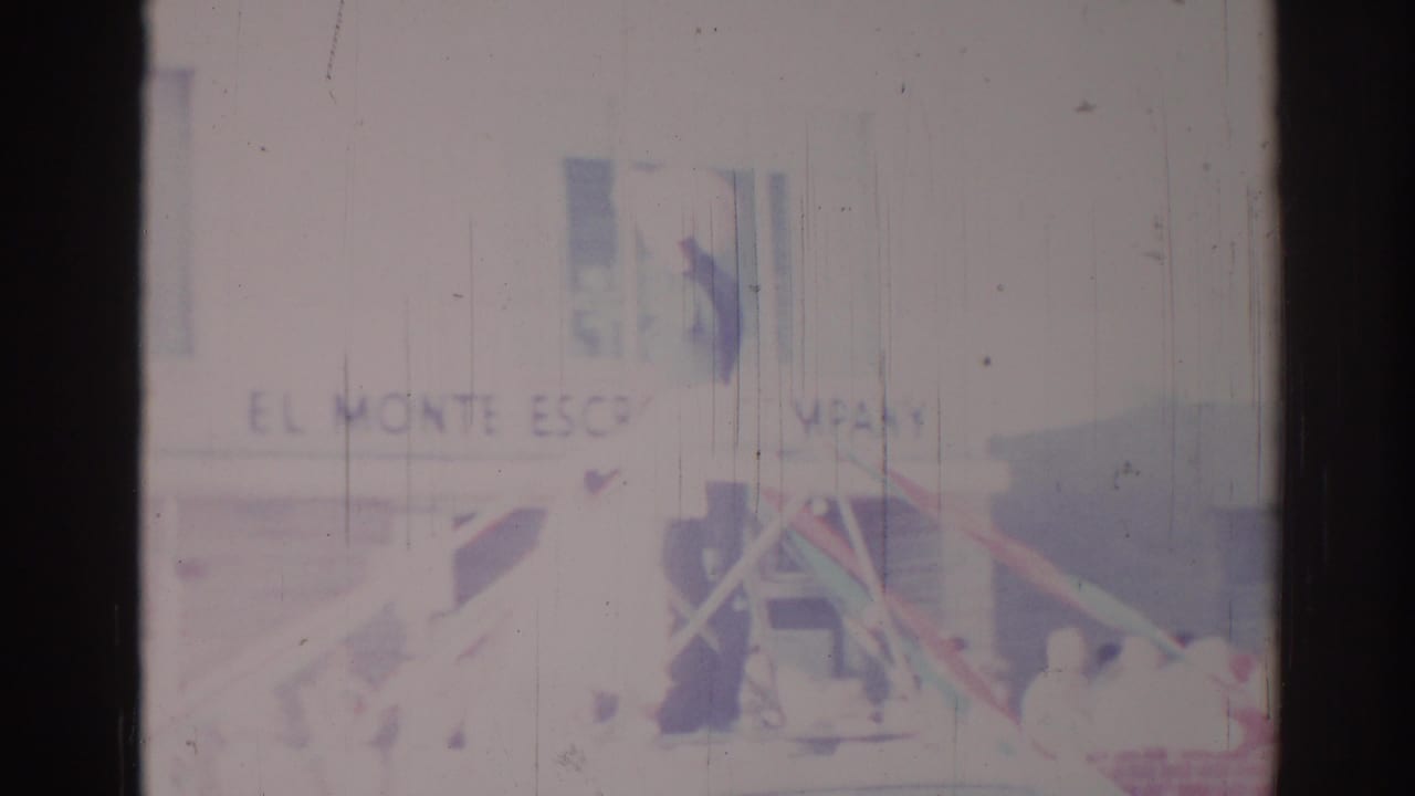 Los Angeles parade home-movie frame showing Monte Escrow Company signage, float structure, and people along the street.
