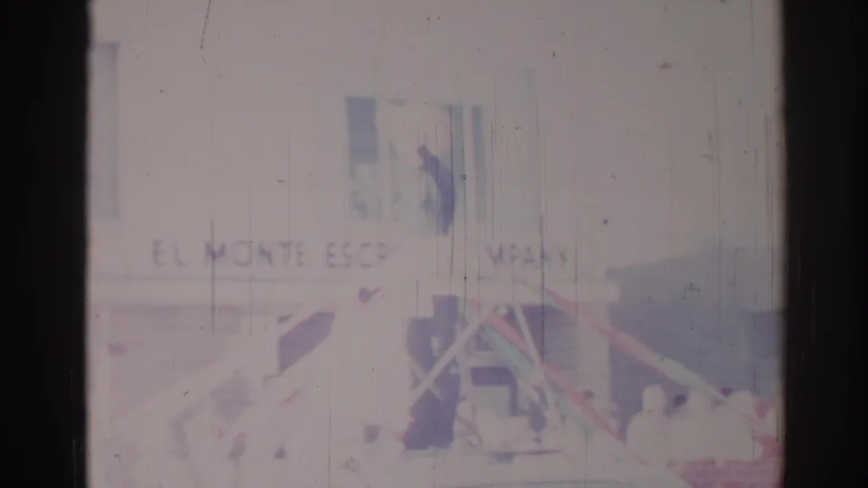 Los Angeles parade home-movie frame showing Monte Escrow Company signage, float structure, and people along the street.
