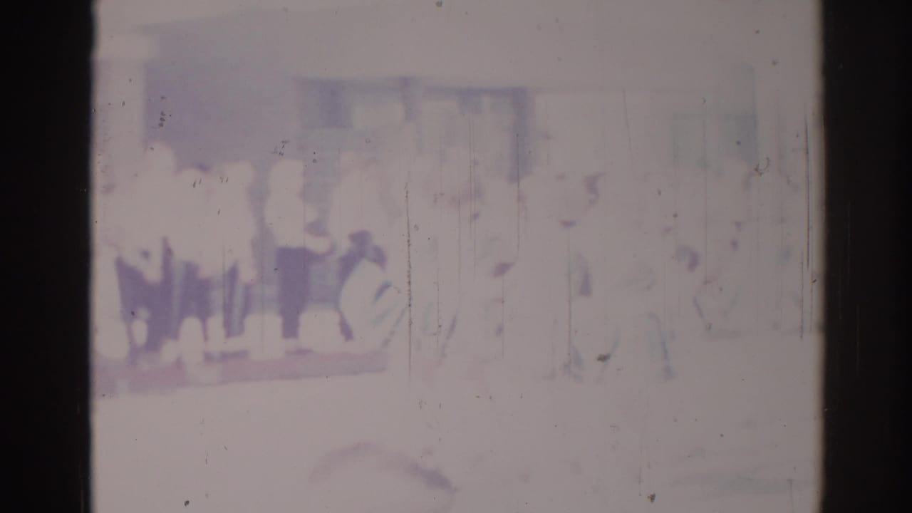 Soft 8mm frame from Los Angeles in 1967 with indistinct people standing or marching in a grouped line.