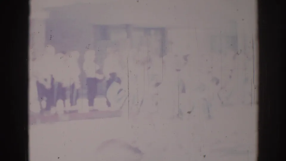 Soft 8mm frame from Los Angeles in 1967 with indistinct people standing or marching in a grouped line.