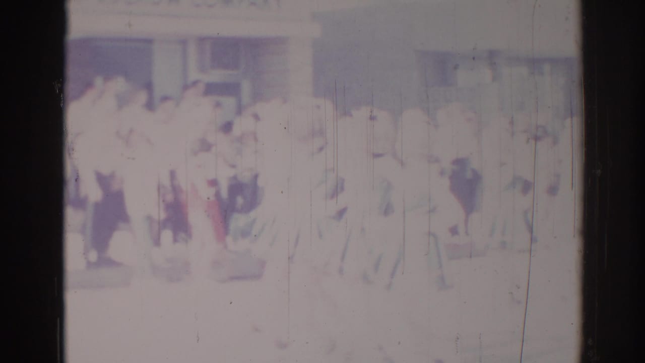Faded 1967 Los Angeles home-movie frame showing a larger formation of people in light clothing moving past the camera.