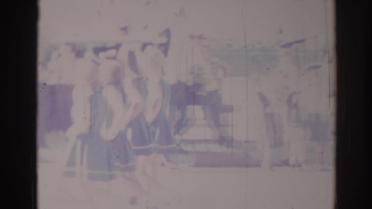 Soft 1967 Los Angeles 8mm frame with people in formation near an unclear urban structure and heavy film fading.
