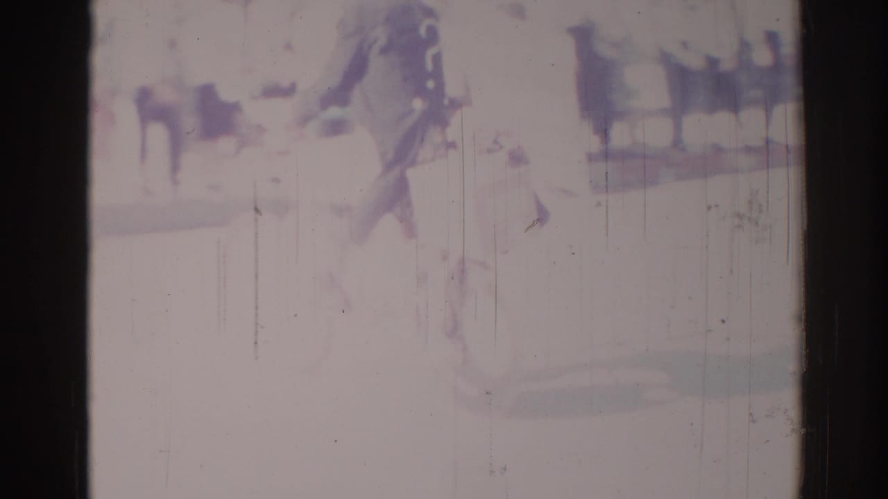 Overexposed 8mm frame with blurred dark figures near a stage-like area.