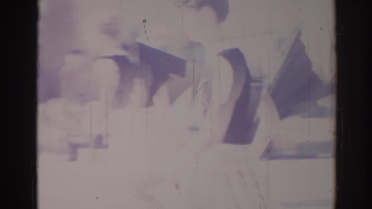 Late-1960s Los Angeles 8mm frame with indistinct dark stage objects and a faint person-shaped form under heavy exposure.
