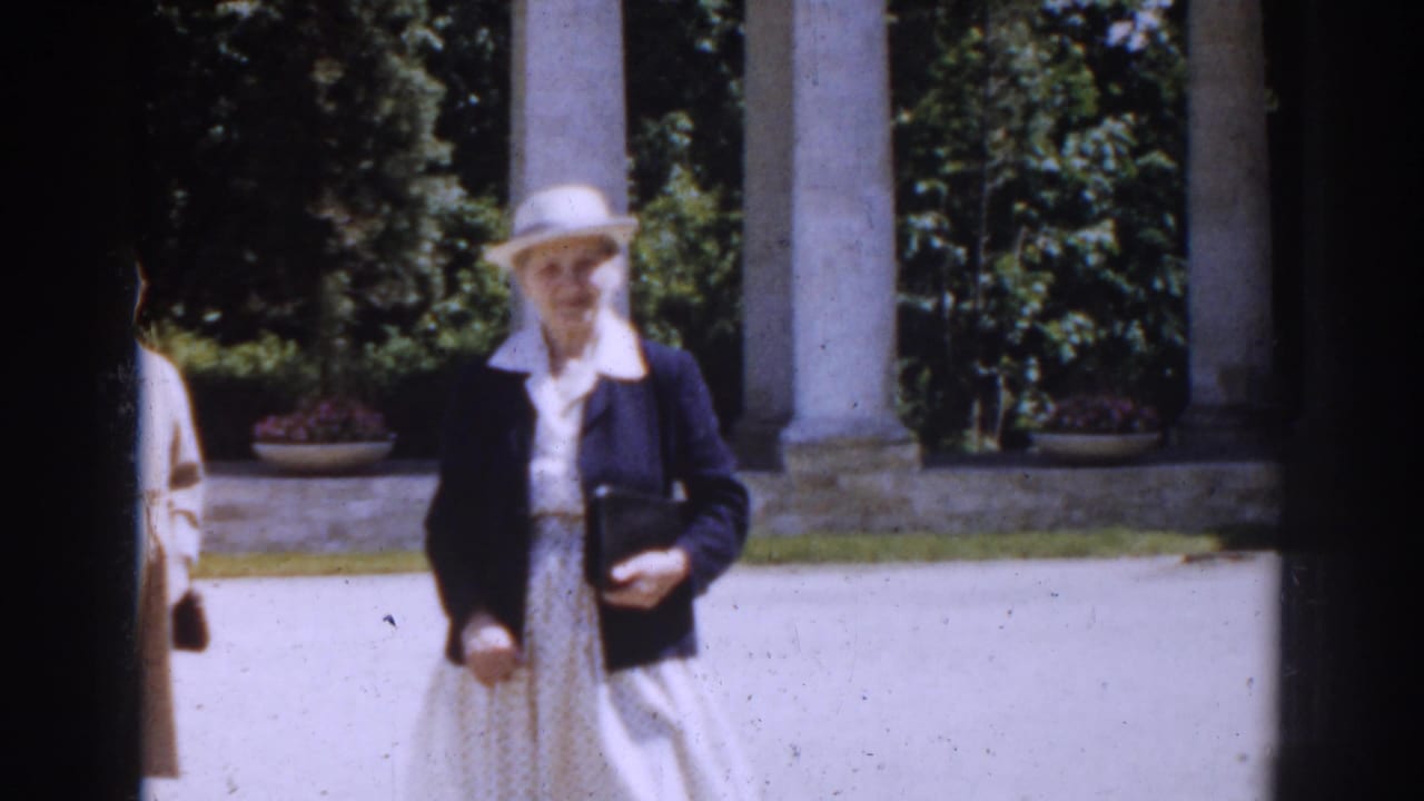 Woman in white hat and dark jacket walking in front of columns.