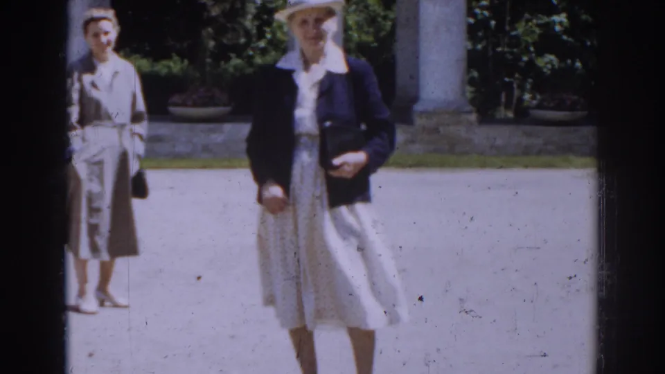Two adult women in 1968 Moscow stand or walk in a bright courtyard, with columns, potted plants, trees, and visible film grain behind them.