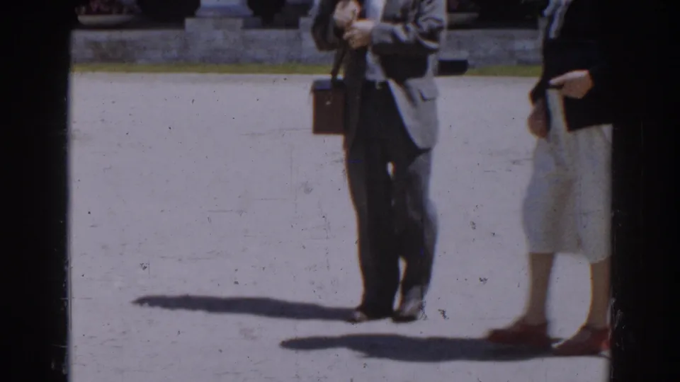 Cropped 1968 Moscow frame showing adults crossing sunlit paving, including a man with a briefcase and a woman in a light skirt.