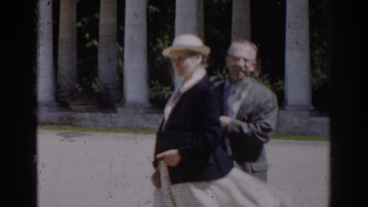In 1968 Moscow home-movie footage, a woman in a light hat and dark jacket walks past tall columns with another adult nearby.
