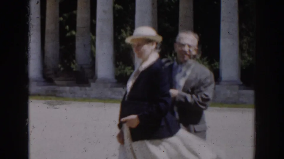 In 1968 Moscow home-movie footage, a woman in a light hat and dark jacket walks past tall columns with another adult nearby.