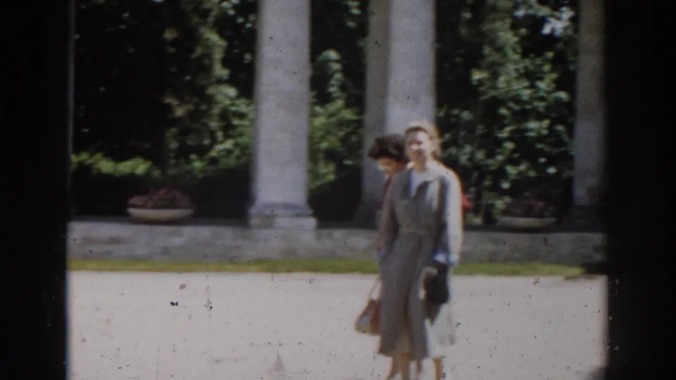 Two women pause or walk near pale classical columns and dense greenery in the 1968 Moscow park footage.