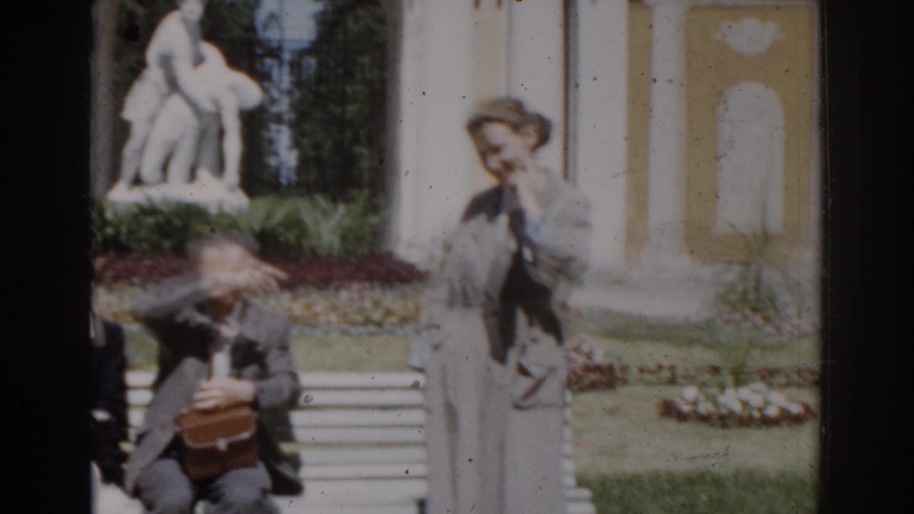 Standing woman near a bench as a seated man adjusts a small brown bag.