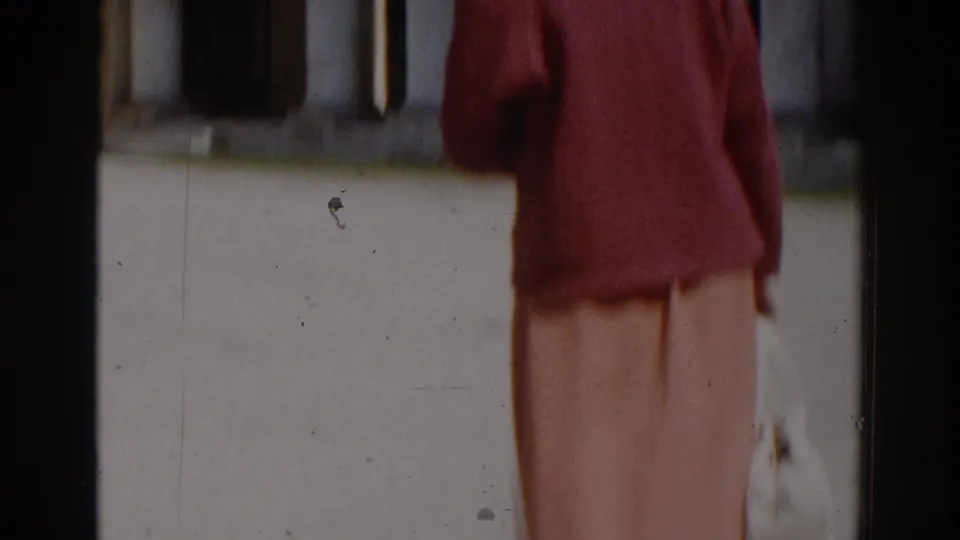 In 1968 Moscow home-movie footage, a woman in a red sweater and peach skirt walks through a sunlit courtyard.