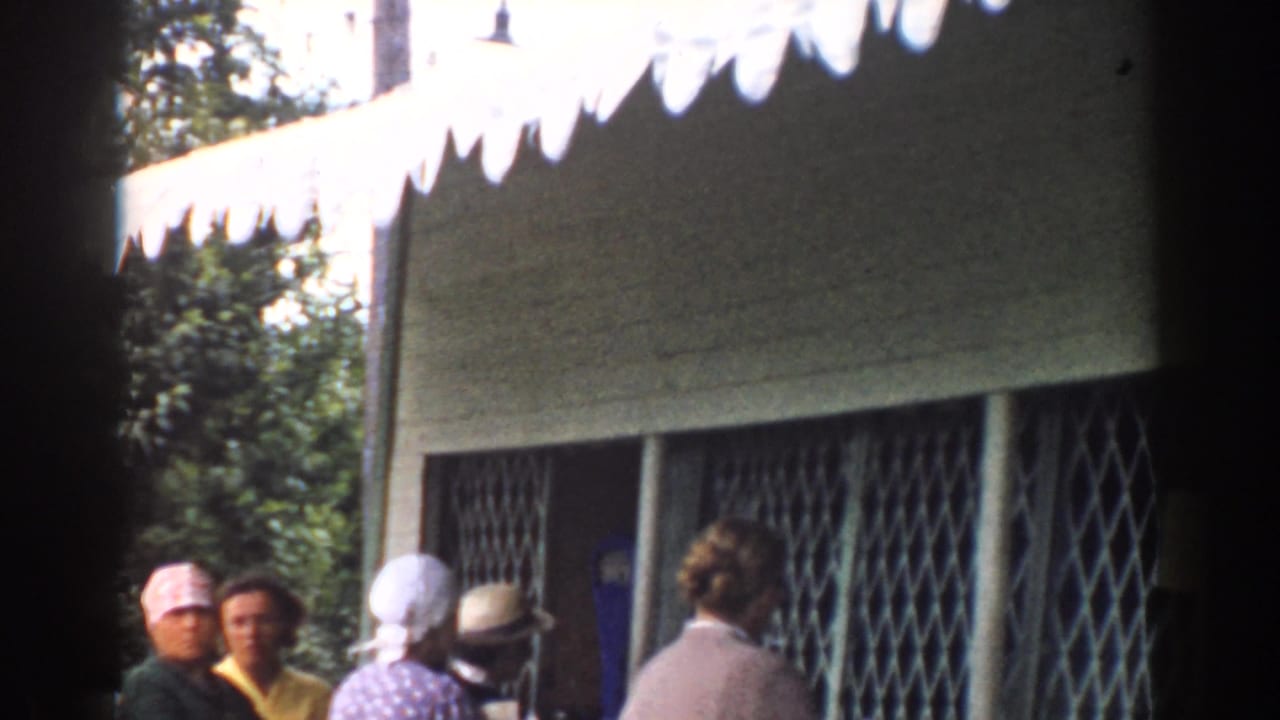 People gathered near a restaurant window with a metal grille and awning.