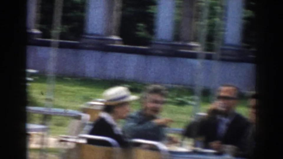 Adults in period clothing sit at a white outdoor table in Moscow, with drinks, chairs, greenery, and columns behind them.