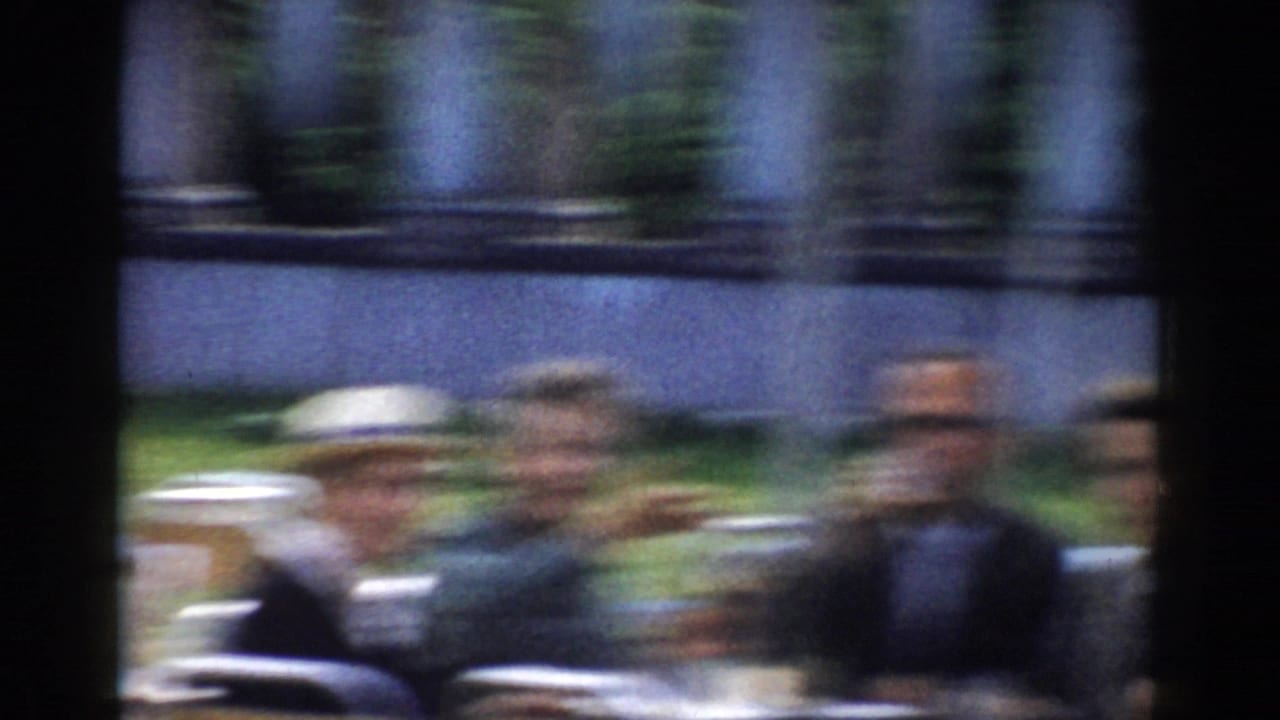 Blurred adults seated outdoors at a white table under a striped awning.