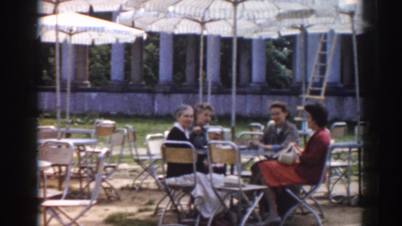 Four women seated at an outdoor cafe table under white umbrellas.