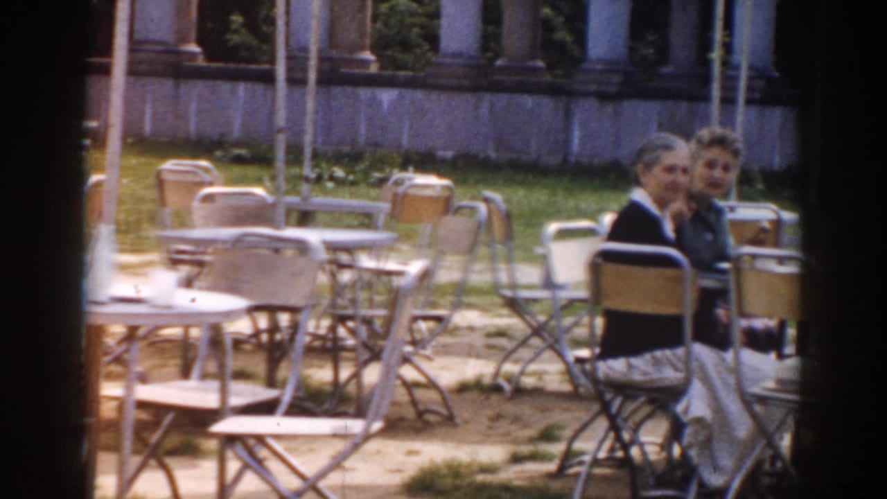 Two women seated at an outdoor cafe table with empty chairs nearby.
