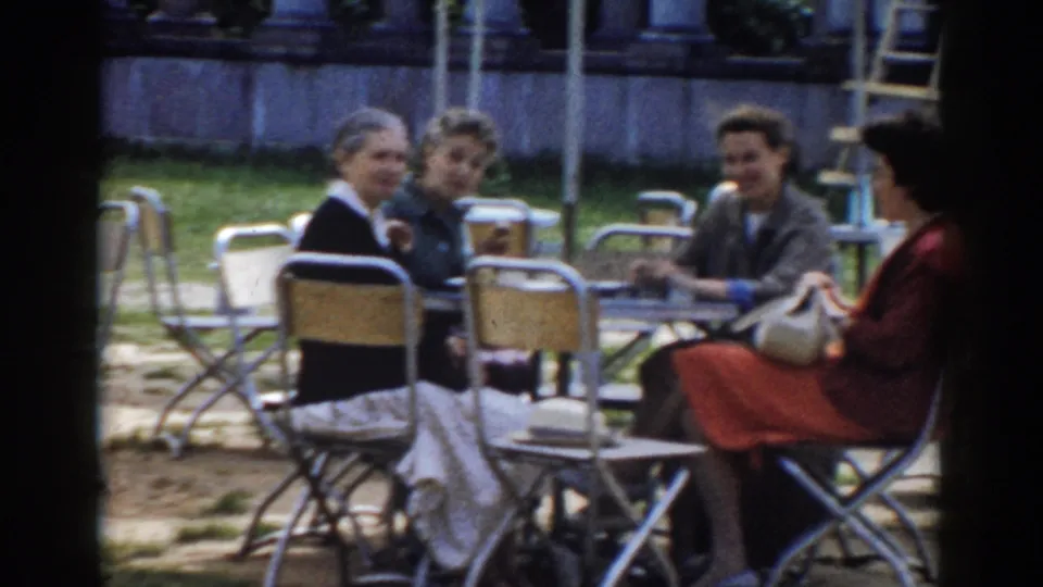 Four adults sit around outdoor cafe tables in Moscow, with one woman holding a handbag and others turned toward the camera.