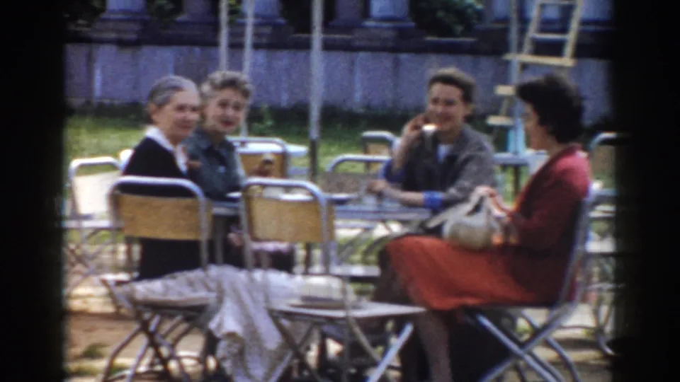 At an outdoor Moscow cafe table, adults sit together as a man raises a cup and two women face the camera.