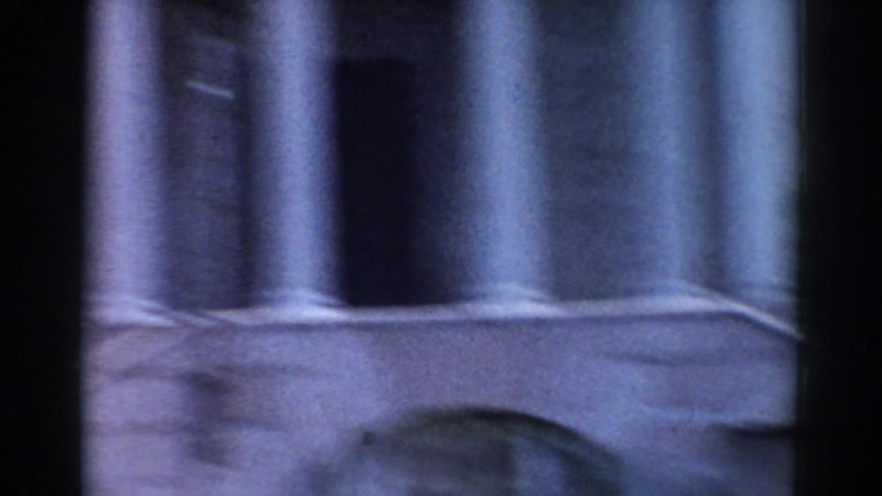 1968 Moscow home-movie frame showing fluted columns and a partial arched stone facade in soft, faded color.