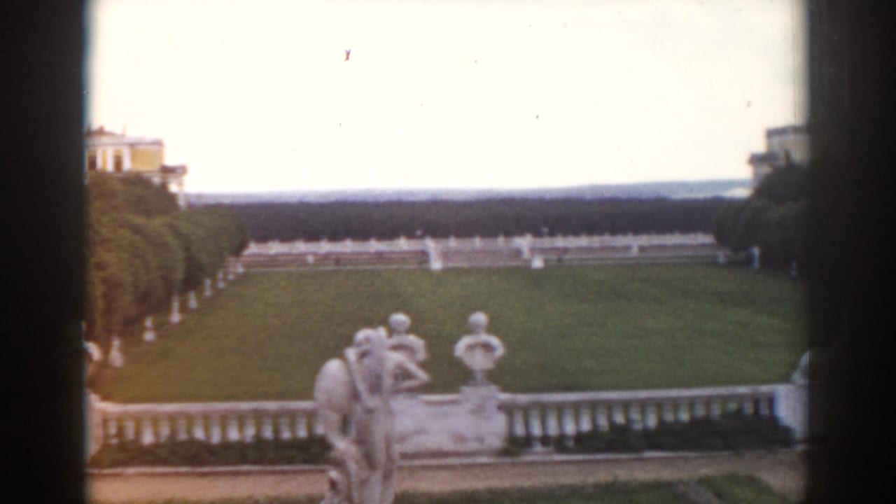 Stone sculptures and balustrade overlook a broad formal garden with distant palace buildings.