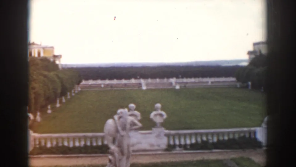 1968 Moscow 8mm frame showing classical garden sculptures, a terrace balustrade, lawn, trees, and distant palace architecture.