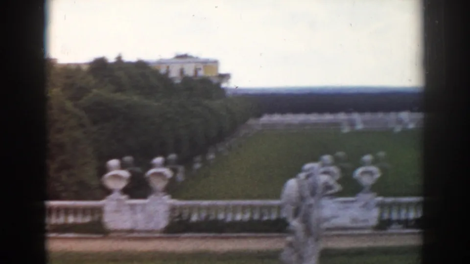 1968 Moscow home-movie view across terrace statuary toward a clipped lawn, hedges, trees, and distant palace structures.