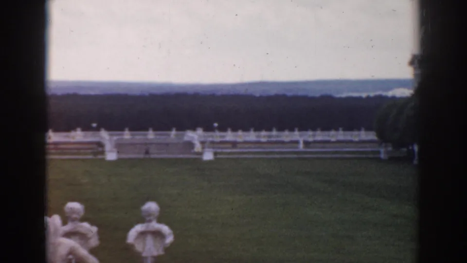 1968 Moscow garden view with a broad lawn, white railing, small classical figures, distant woods, and a dark central film or window edge.