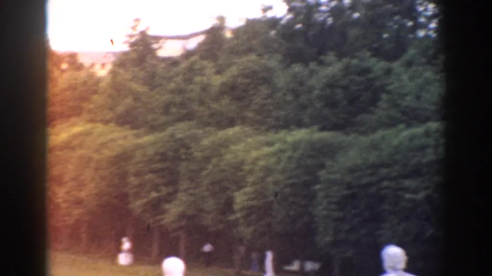 1968 Moscow garden detail with dense hedges, trees, small pale statues, warm exposure flare, and soft 8mm color.