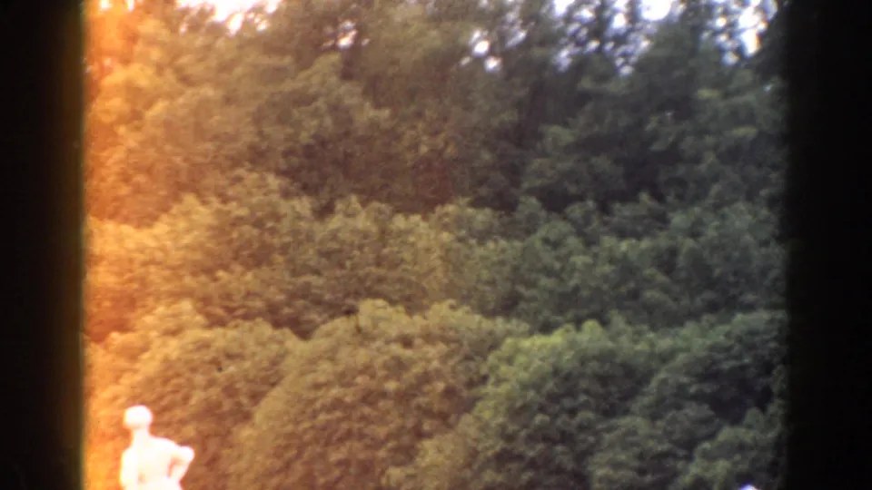 1968 Moscow 8mm frame with a bright garden statue, dense greenery, and warm orange exposure flare along the film edge.