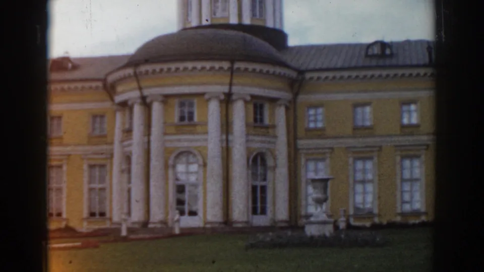 1968 Moscow home-movie frame of a yellow building facade with white columns, a rounded rotunda, tall windows, and a lawn statue.