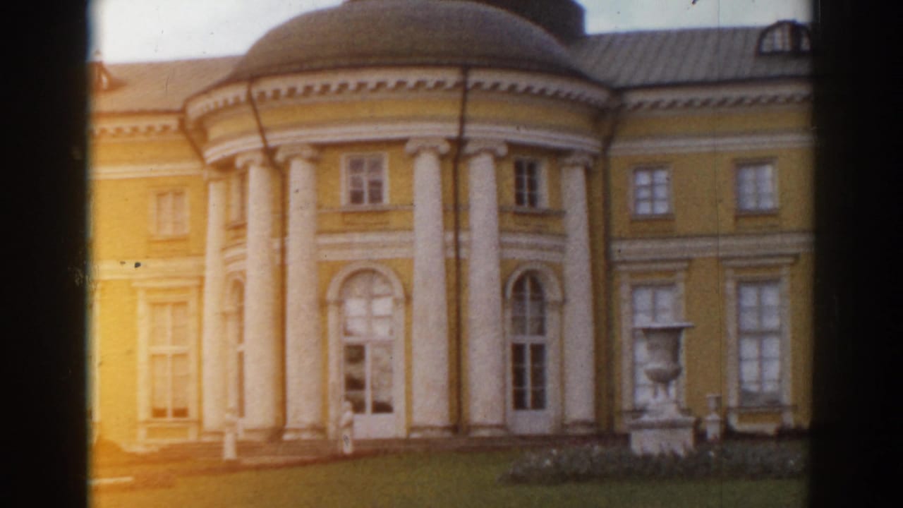 Yellow classical building with columns, rounded roof section, lawn, and dark film borders.