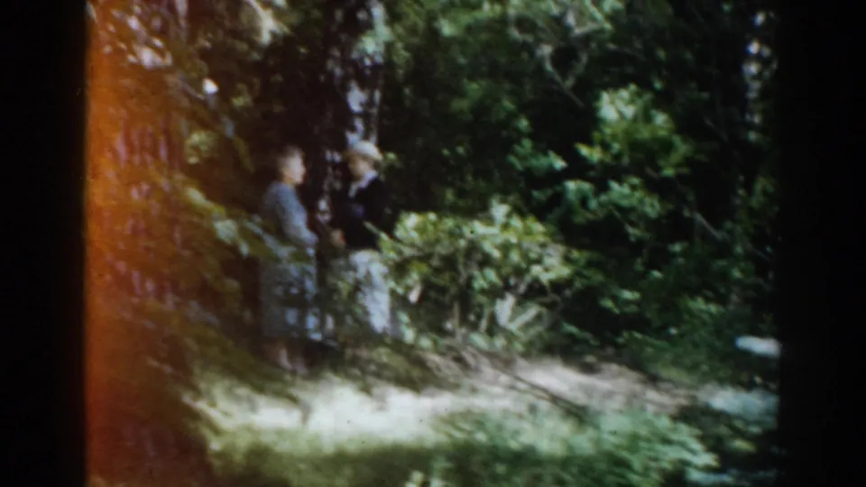 1968 Moscow home-movie frame of two people walking along a bright wooded path bordered by dense green foliage.