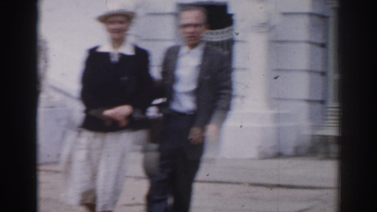 In metadata-supported 1968 Moscow footage, an older woman in a light hat and a man in glasses walk near a pale exterior wall.