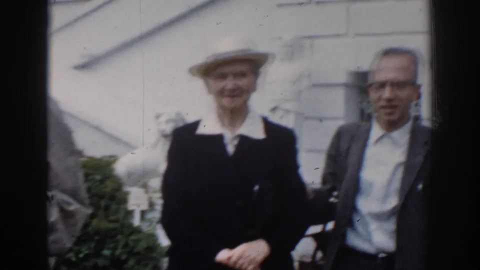 The older couple stands close to the handheld camera in the 1968 Moscow footage, with pale masonry and greenery behind them.