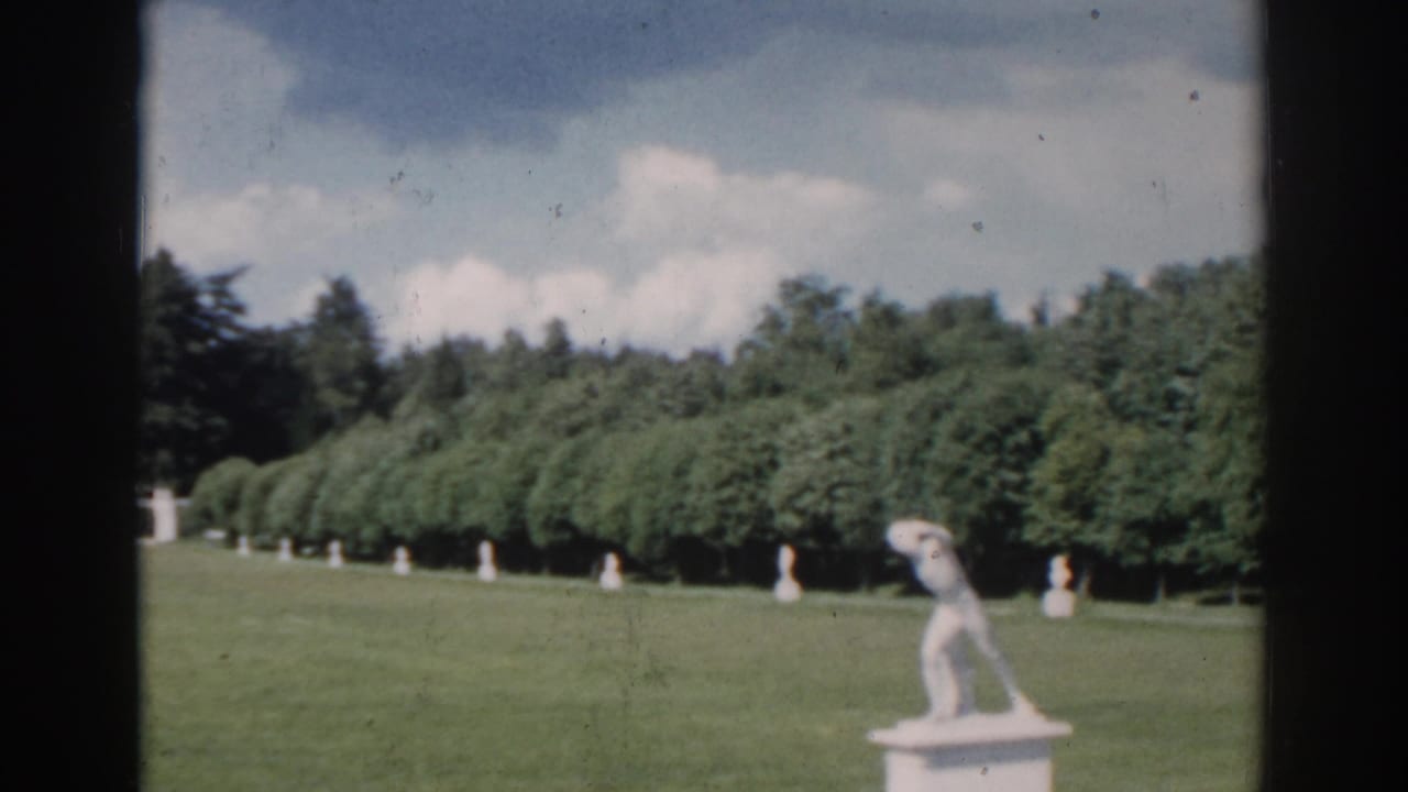 1968 Moscow 8mm frame showing a manicured estate lawn, classical statues, dense trees, and a pale building partly visible beyond the grounds.