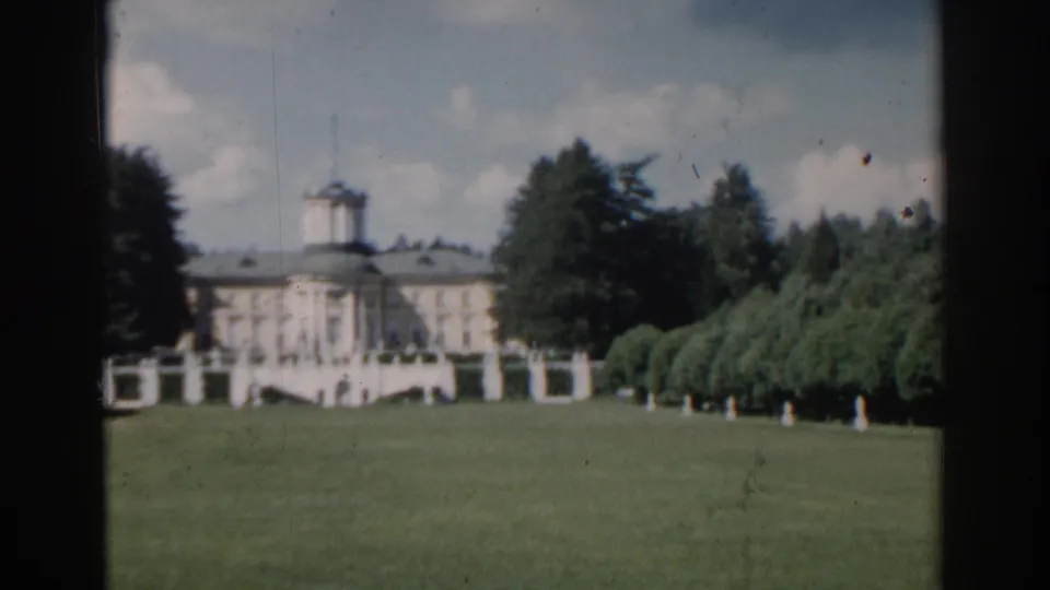 1968 Moscow 8mm frame of a pale mansion and central tower beyond manicured grass, rounded tree rows, garden statues, and distant visitors.