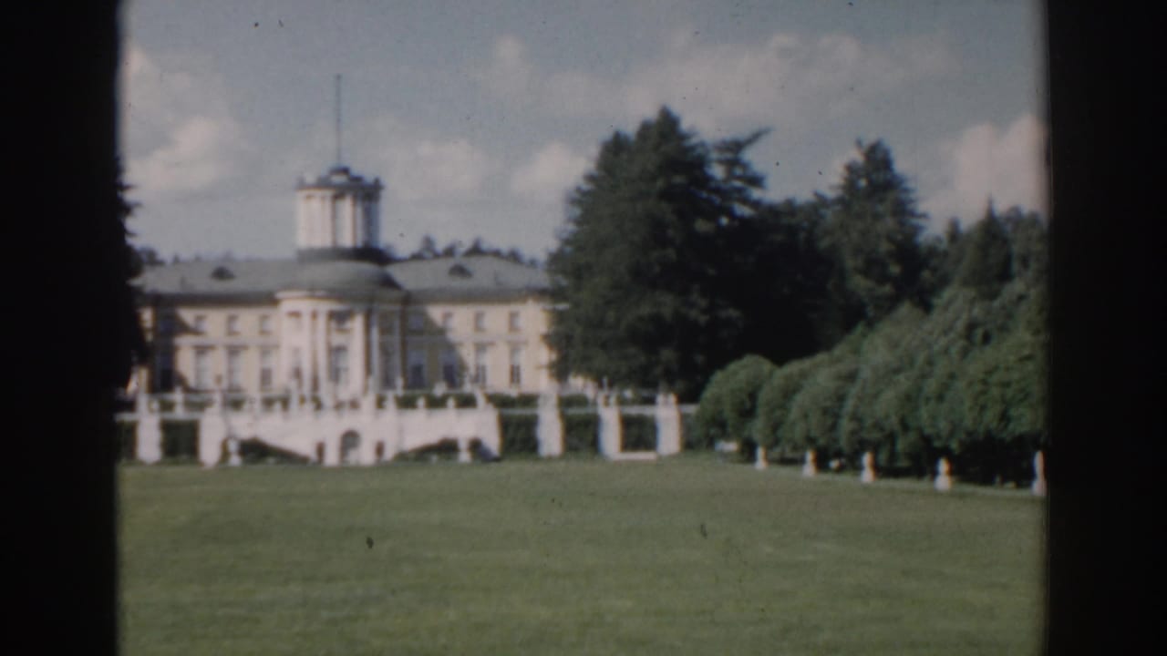 Classical building across a lawn, partly divided by dark vertical frame edges.