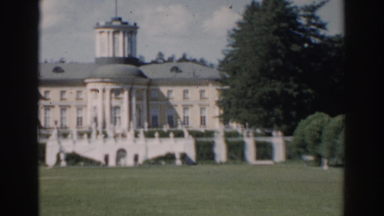 Centered view of a domed classical building with columns and lawn in front.