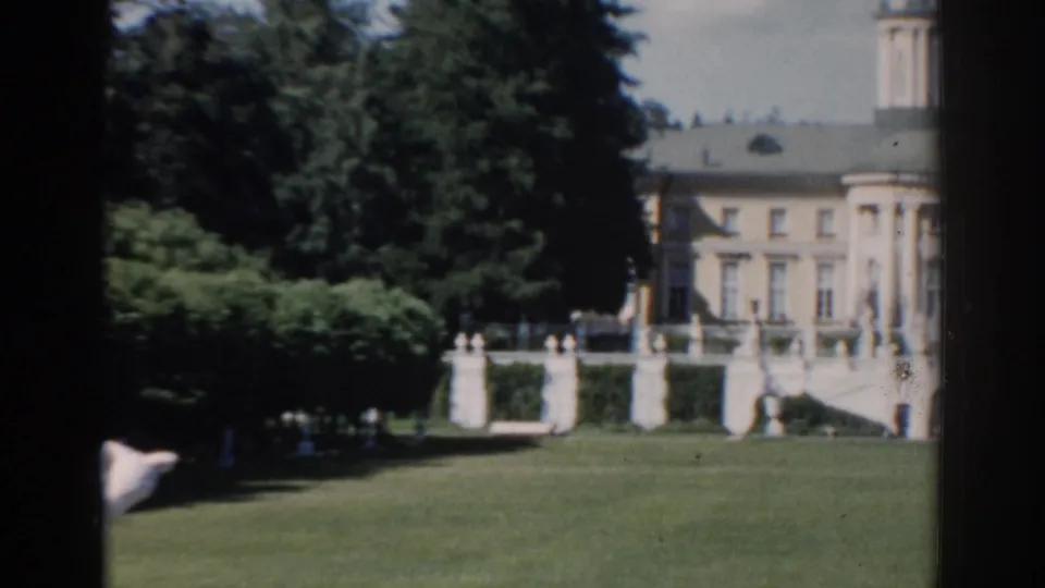 1968 Moscow frame with the building partly cropped at right, dense foliage, white terrace railings, and sunlit grass.