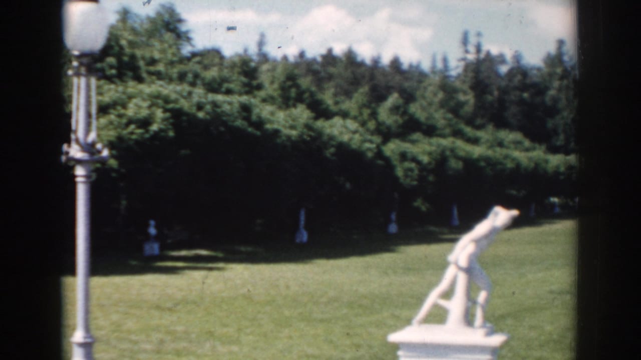 Garden lawn with a lamppost, white statue, trees, and sky.