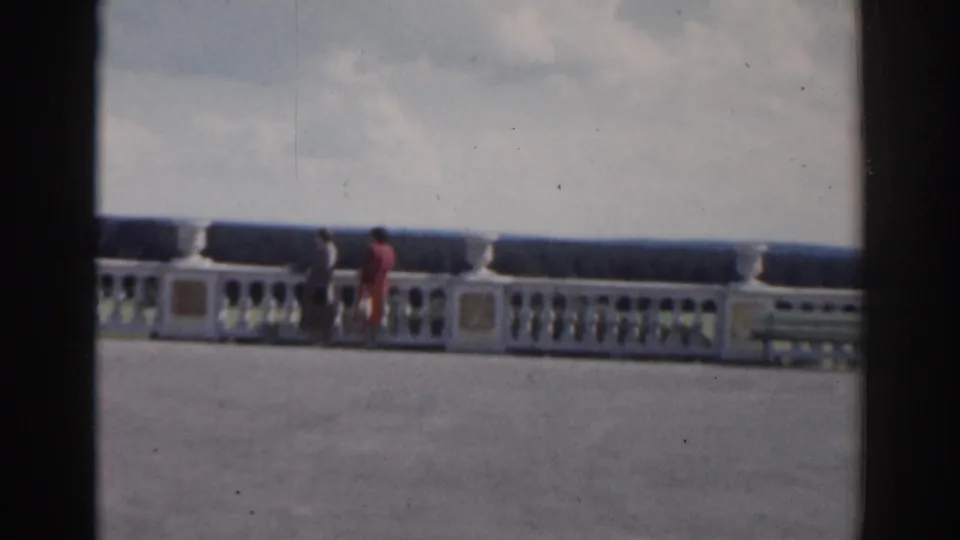 In 1968 Moscow home-movie footage, two women walk along a broad terrace beside a white balustrade with urns and a distant treeline.