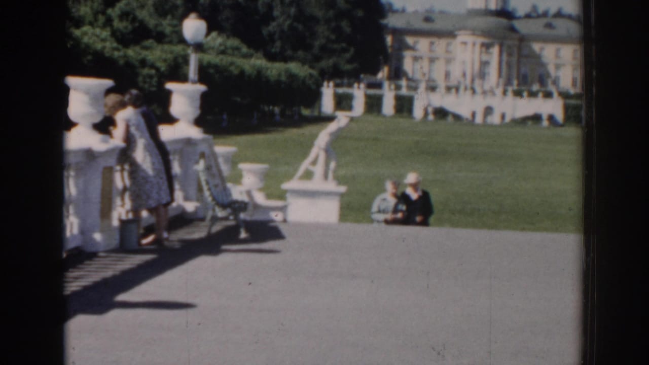 Two women near a terrace and lawn with a large classical building in the background.