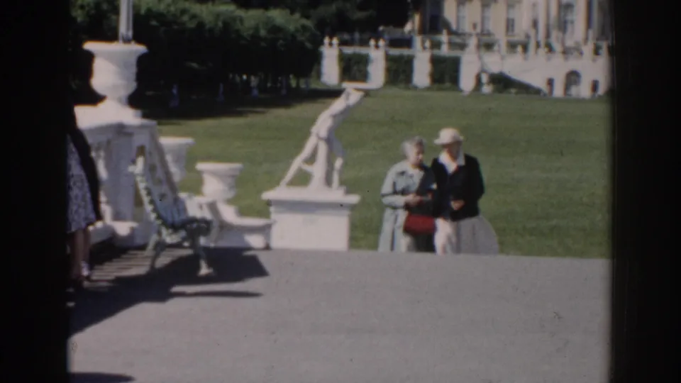 In 1968 Moscow home-movie footage, an elderly couple approaches along a paved garden path near white statuary and a large building.