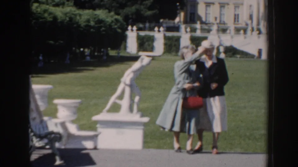Near the end of the clip, the older couple stands or walks close to the camera in the Moscow garden, with the woman lifting a hand near her face.